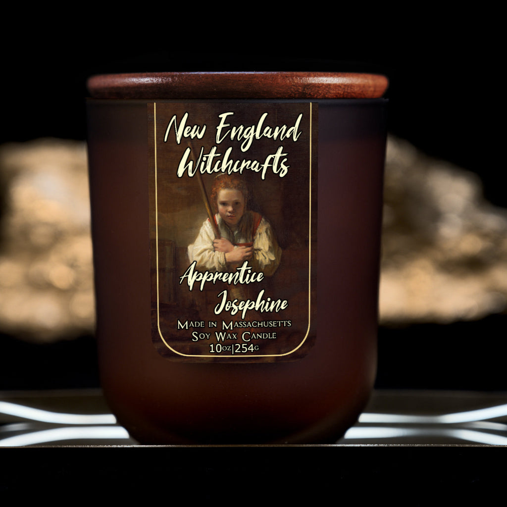 Image depicts a frosted amber candle jar with lid and a label depicting an oil painting of a young witch apprentice holding her broom.