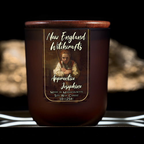 Image depicts a frosted amber candle jar with lid and a label depicting an oil painting of a young witch apprentice holding her broom.
