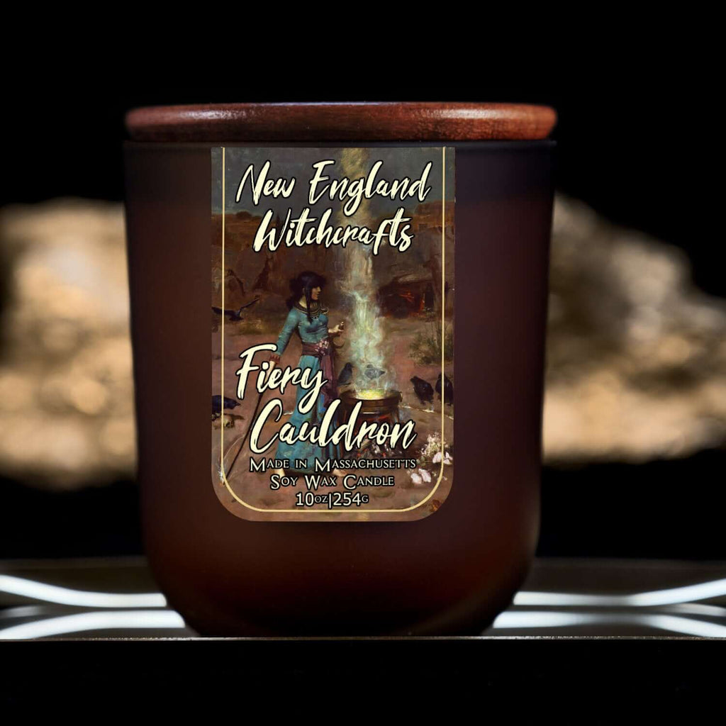 Image depicts a frosted amber candle jar with lid and a label depicting an oil painting of a witch conjuring a spell over a fiery cauldron.