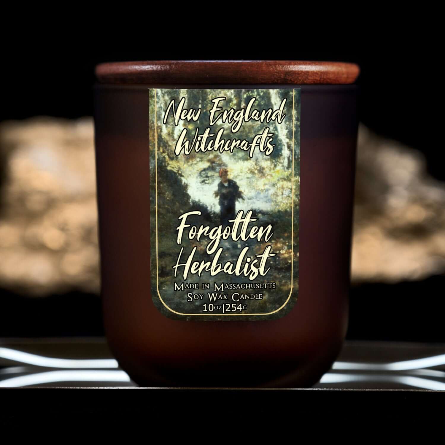 Image depicts a frosted amber candle jar with lid and a label depicting an oil painting of a lone woodsman in the distance.