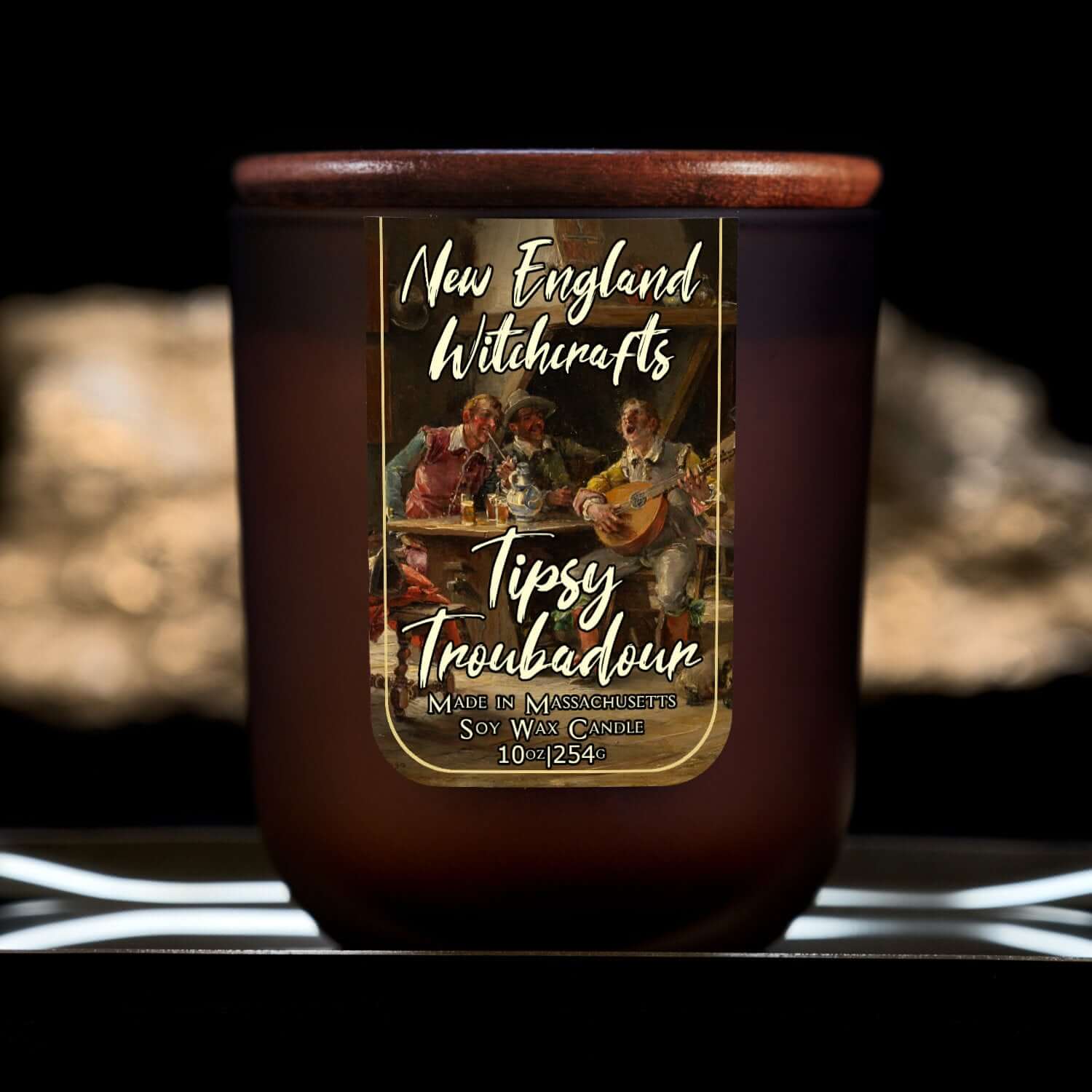 Image depicts a frosted amber candle jar with lid and a label depicting an oil painting of a drunken tavern guest