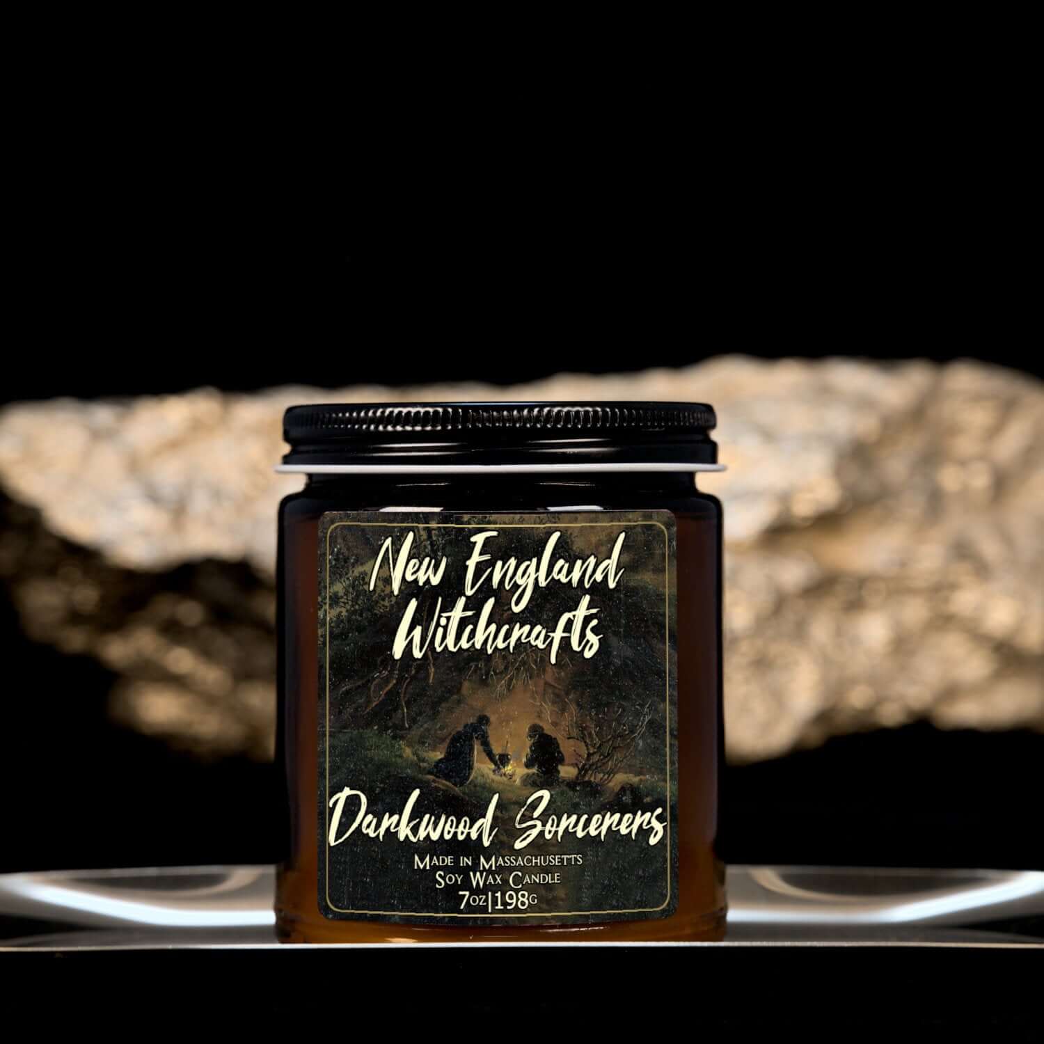 Image depicts an amber candle with black lid, smaller, and a label depicting an oil painting of sorcerers conjuring in secret in the forest.