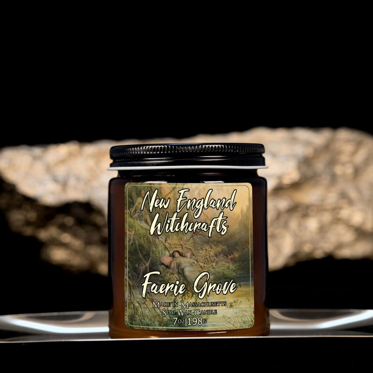 Image depicts an amber candle with black lid, smaller, and a label depicting an oil painting of faeries basking in a grotto.