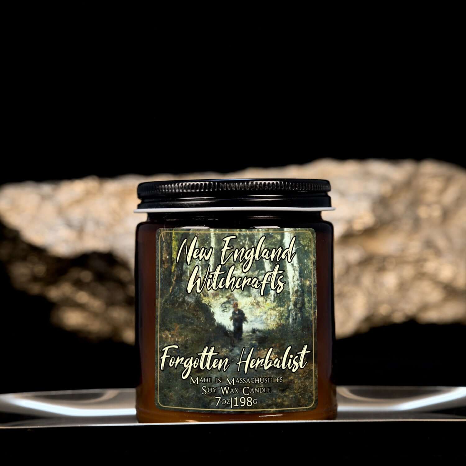 Image depicts an amber candle with black lid, smaller, and a label depicting an oil painting of a lone woodsman in the distance.