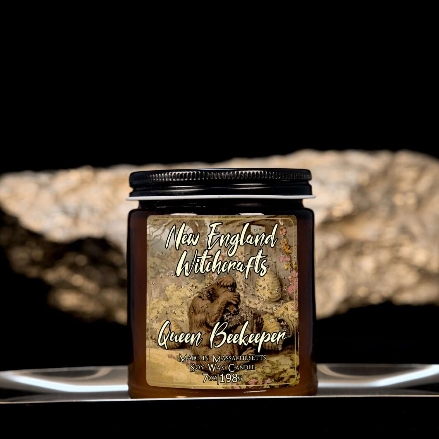 Image depicts an amber candle with black lid, smaller, and a label depicting an oil painting of a bear being attacked by bees.