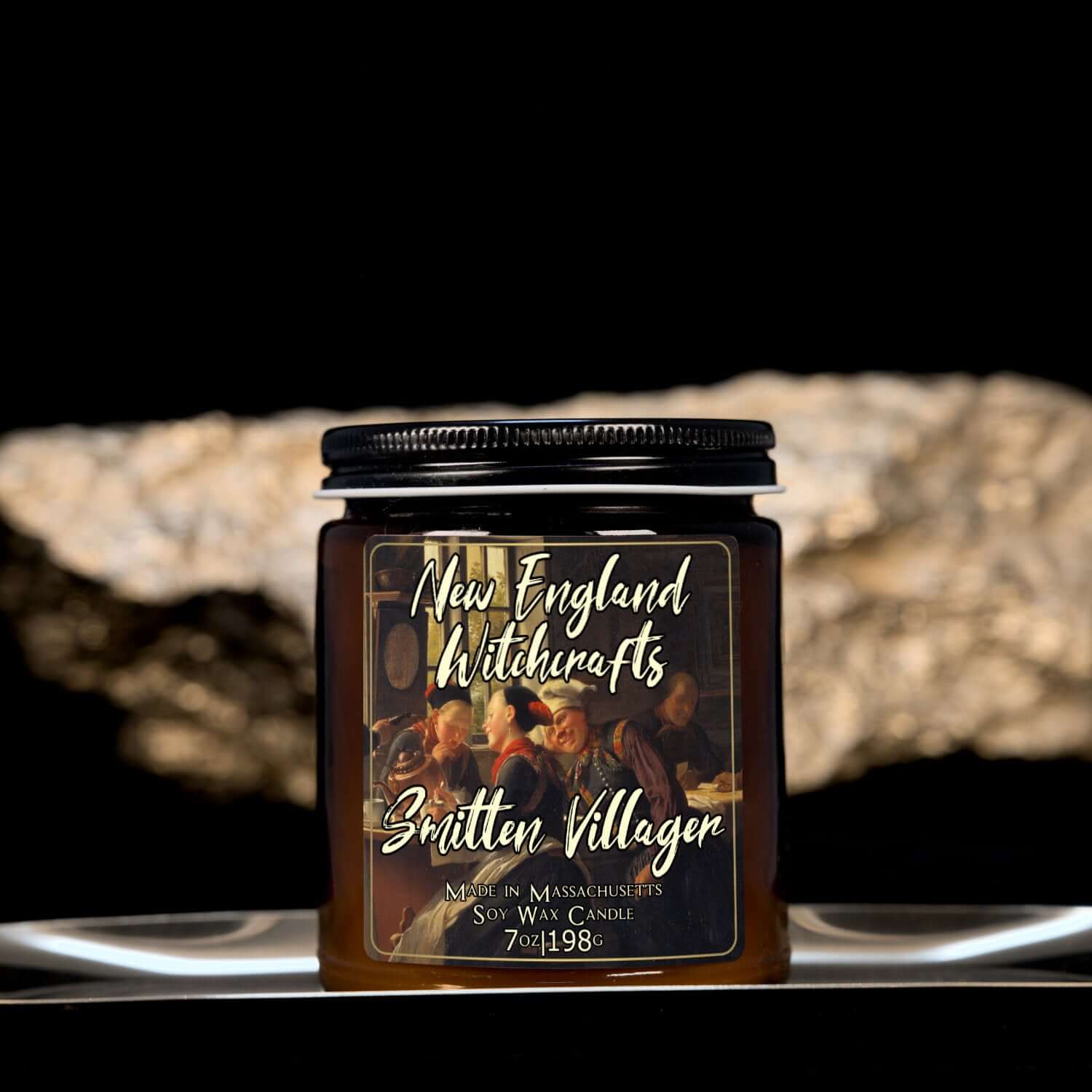 Image depicts an amber candle with black lid, smaller, and a label depicting an oil painting of a lovestruck man.