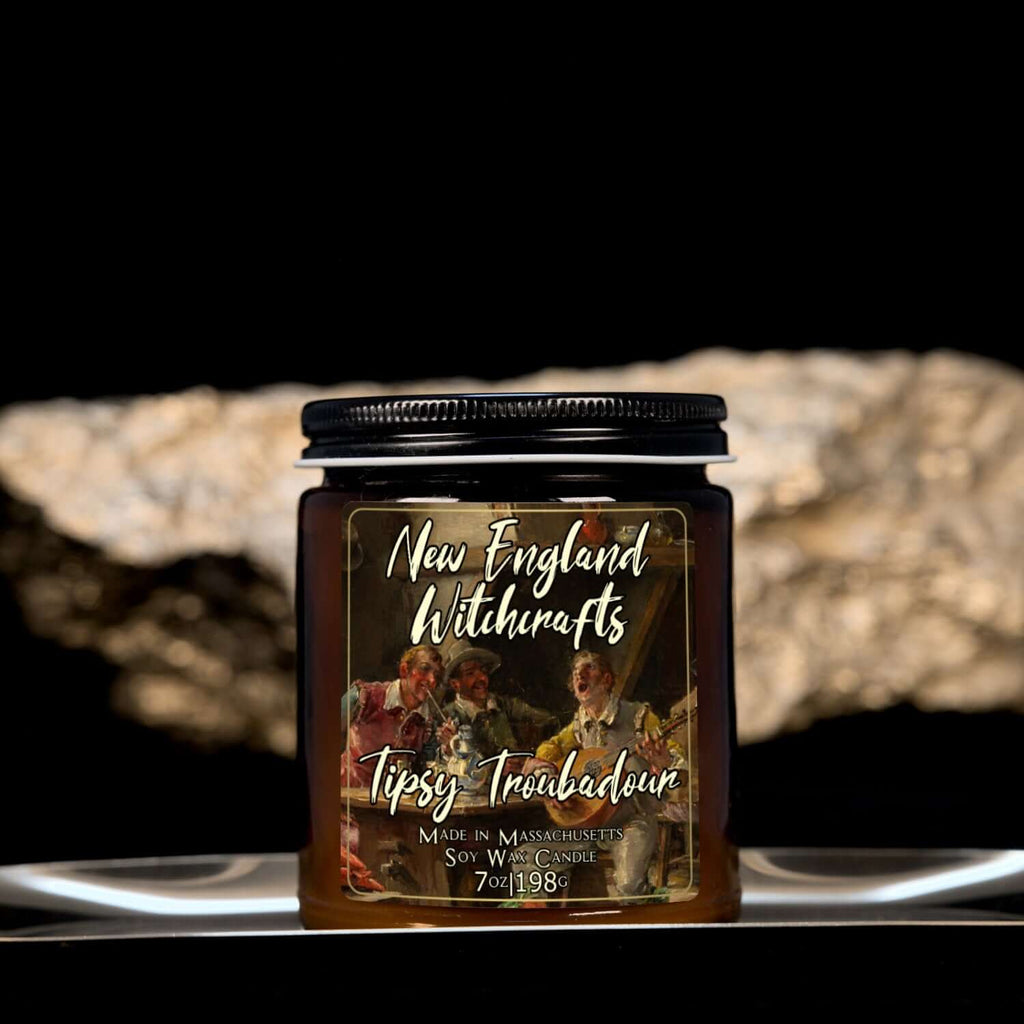 Image depicts an amber candle with black lid, smaller, and a label depicting an oil painting of a drunken tavern guest